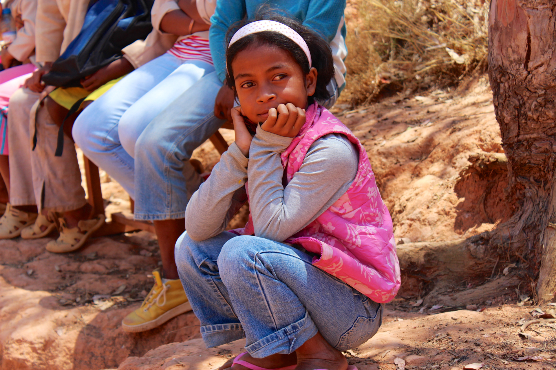 A small girl with blue jeans and a pink jacket sat looking in the distance at the Ambondrona School, Madagascar